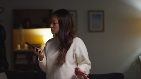 Angry-Anxious-Or-Stressed-Woman-Spending-Evening-At-Home-Standing-In-Lounge-Talking-On-Mobile-Phone